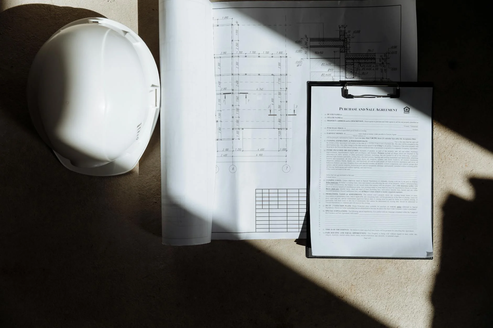 Floor plans, contract documents, and a hard hat on a desk in natural light