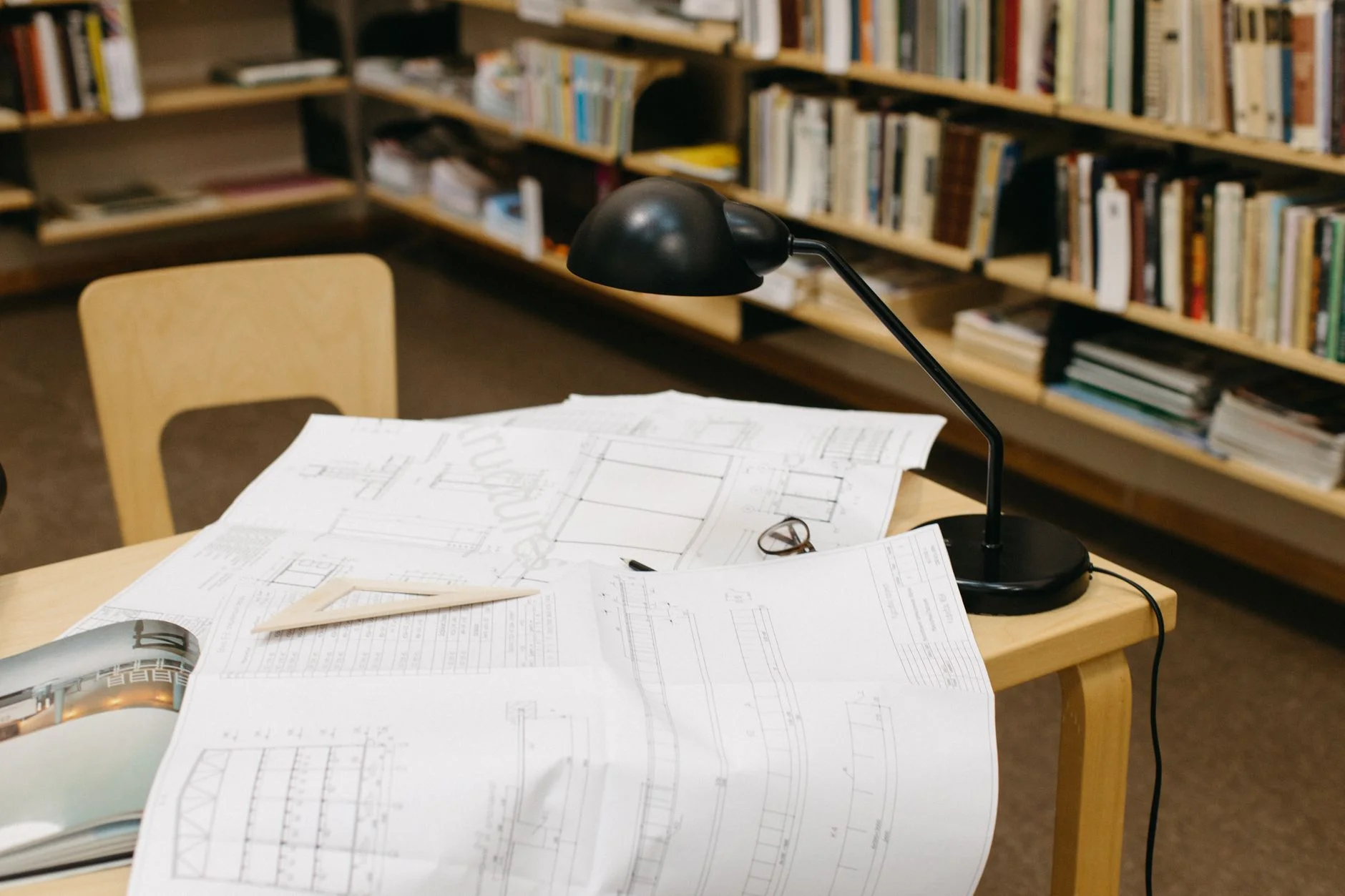 Engineering drawings and technical documents spread across a desk under a work lamp