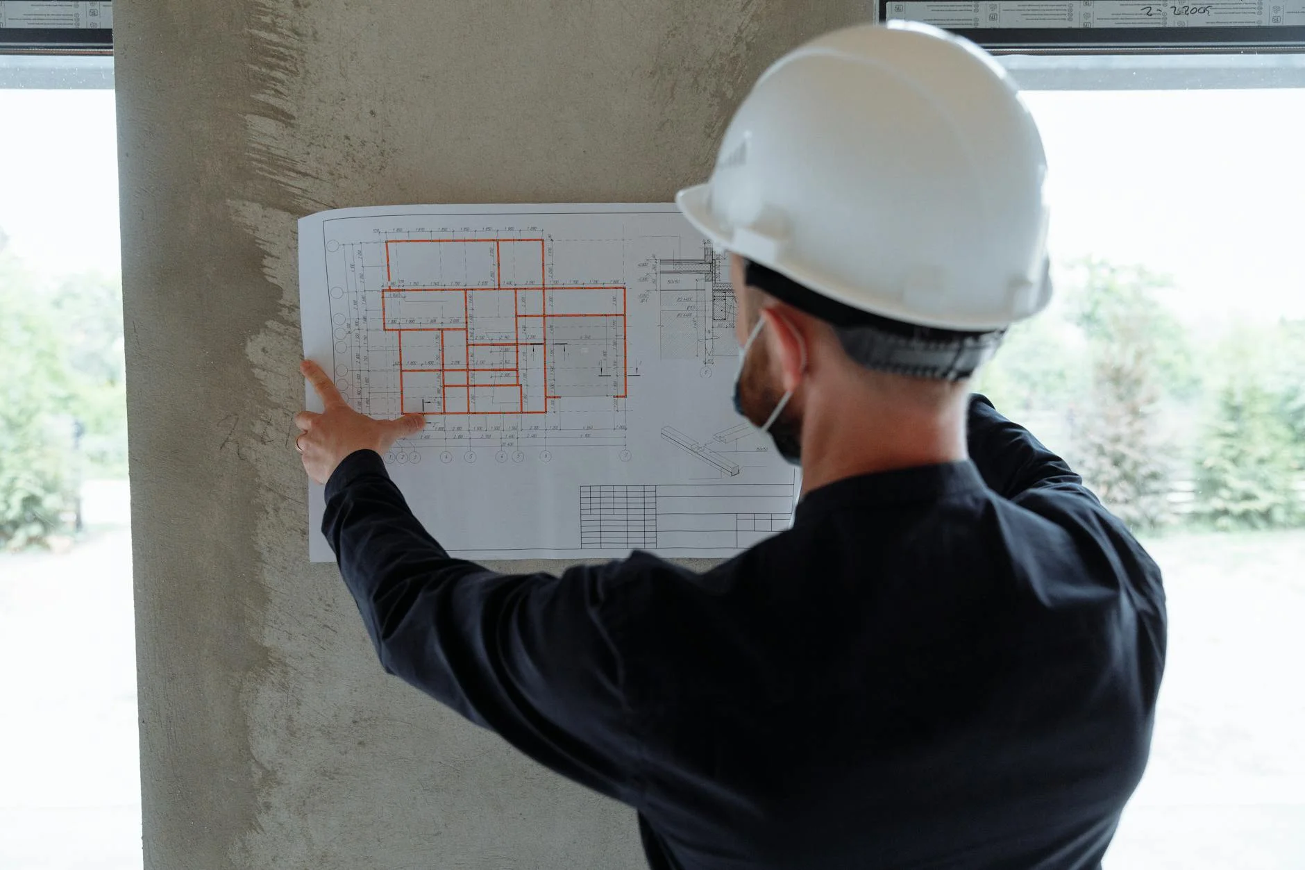 Engineer in a hardhat reviewing large-format engineering drawings at a construction site