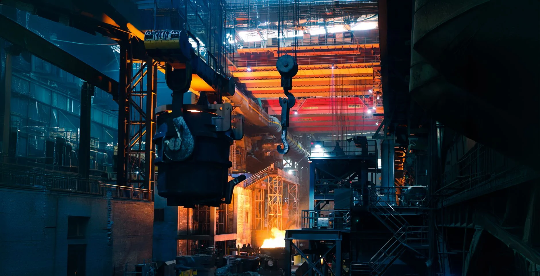 Inside a working steel factory with overhead cranes and molten metal casting an intense glow, the kind of supplier operation vendor qualification is meant to vouch for