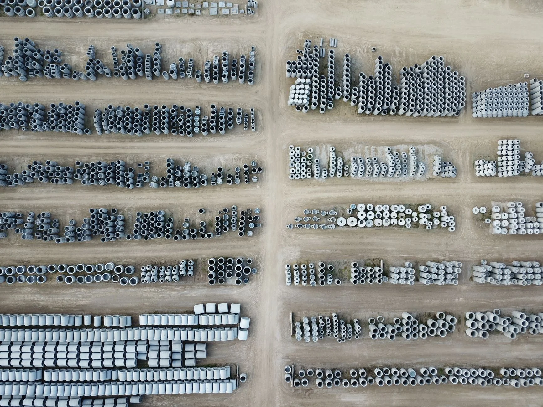 Aerial view of concrete pipes organized in rows across an outdoor storage yard